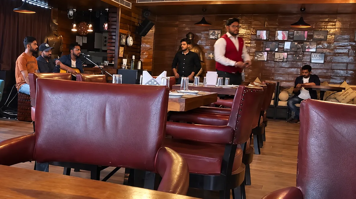 Musicians playing an acoustic live set in the BAR CODE dining room, with leather chairs in the foreground.